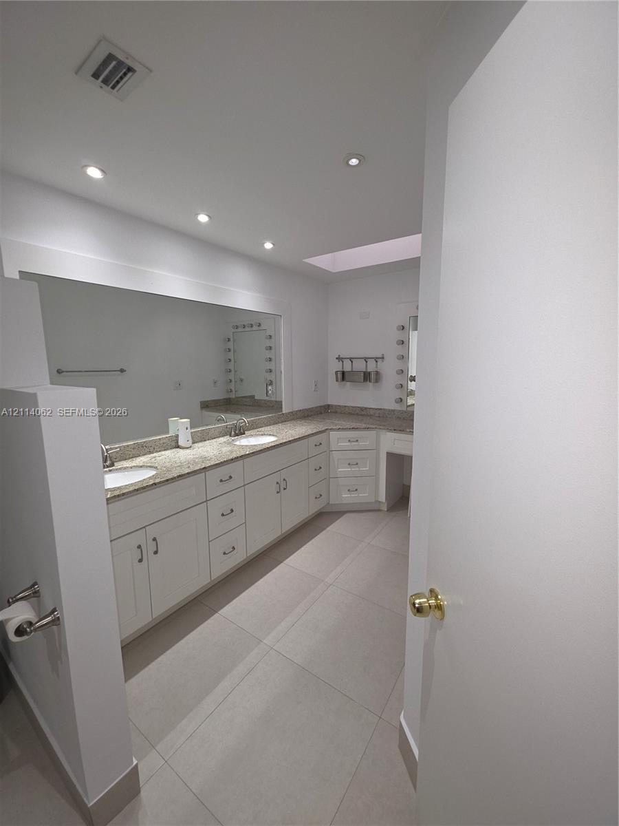 Bathroom featuring a dual-sink vanity with stone countertops, white cabinetry, a skylight, and tile flooring