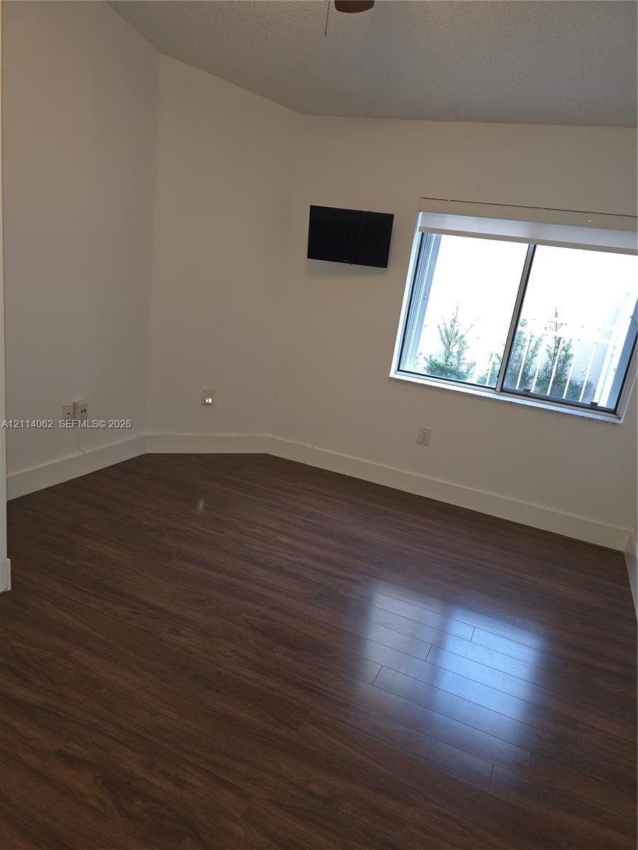 Room featuring wood-finish flooring, white walls, and a sliding window with installed roller shade