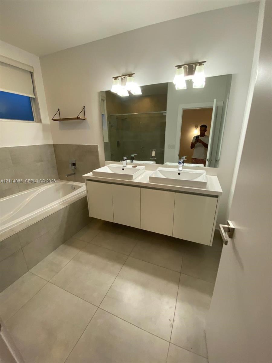 Floating white vanity with double rectangular vessel sinks, quartz countertop, oversized wall-mounted mirror, and tile-surround soaking tub