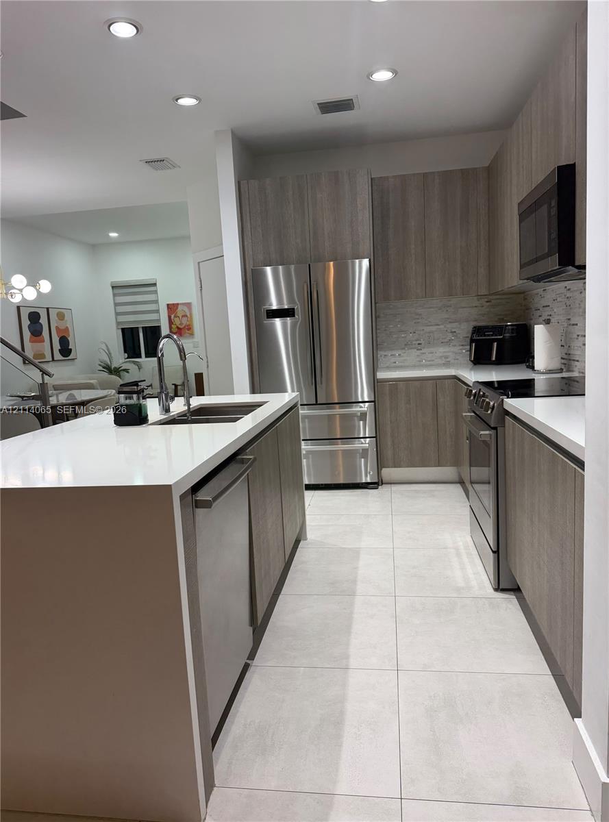 Kitchen featuring flat-panel cabinetry, a quartz waterfall island, large-format tile flooring, stainless steel appliances, and recessed lighting