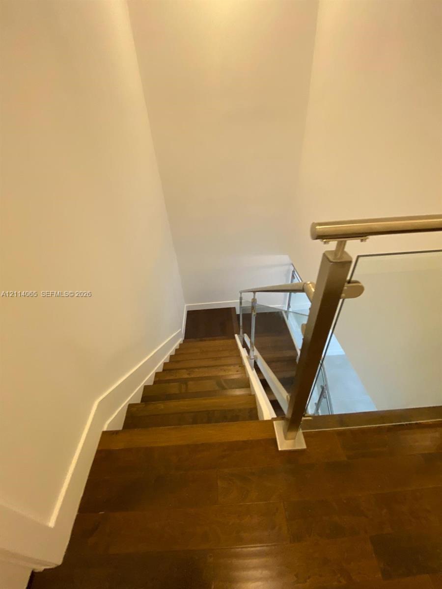 Staircase featuring wood-finish flooring, a stainless steel handrail, and tempered glass paneling