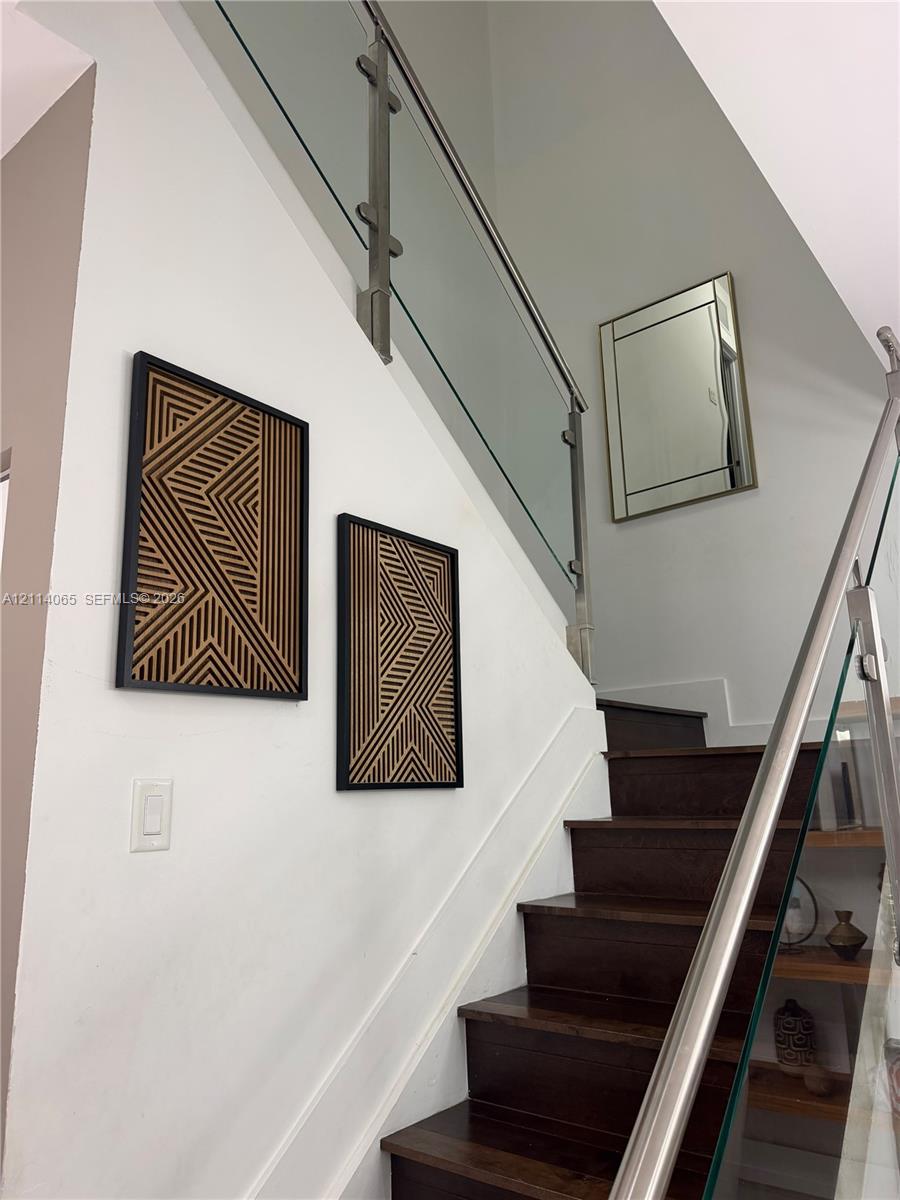 Staircase featuring dark-tone wood treads, a glass railing system, and a metallic handrail