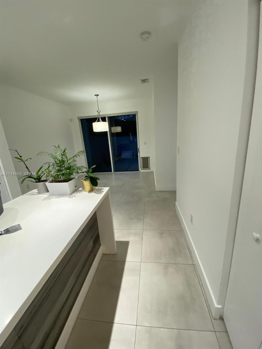 Kitchen island featuring a solid white countertop and wood-finish cabinetry, complemented by large-format tile flooring, a hanging pendant light fixture, and sliding glass doors