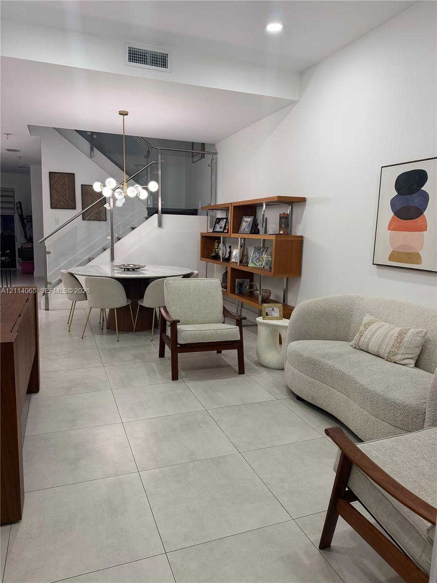 Open-concept interior featuring large-format tile flooring, recessed lighting, and a contemporary staircase with glass paneling and a metal handrail