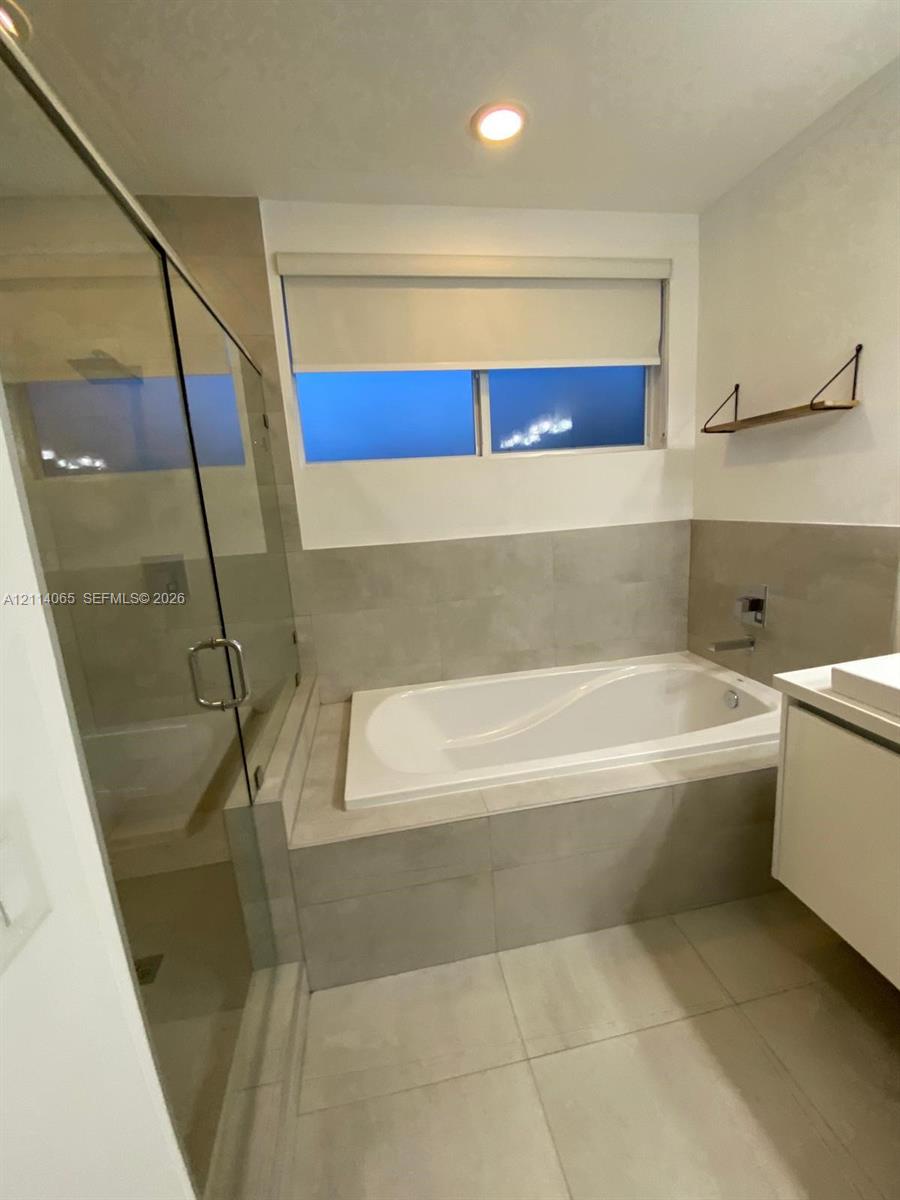 Soaking tub with a tile surround, glass-enclosed shower, large-format floor tiling, and a floating vanity