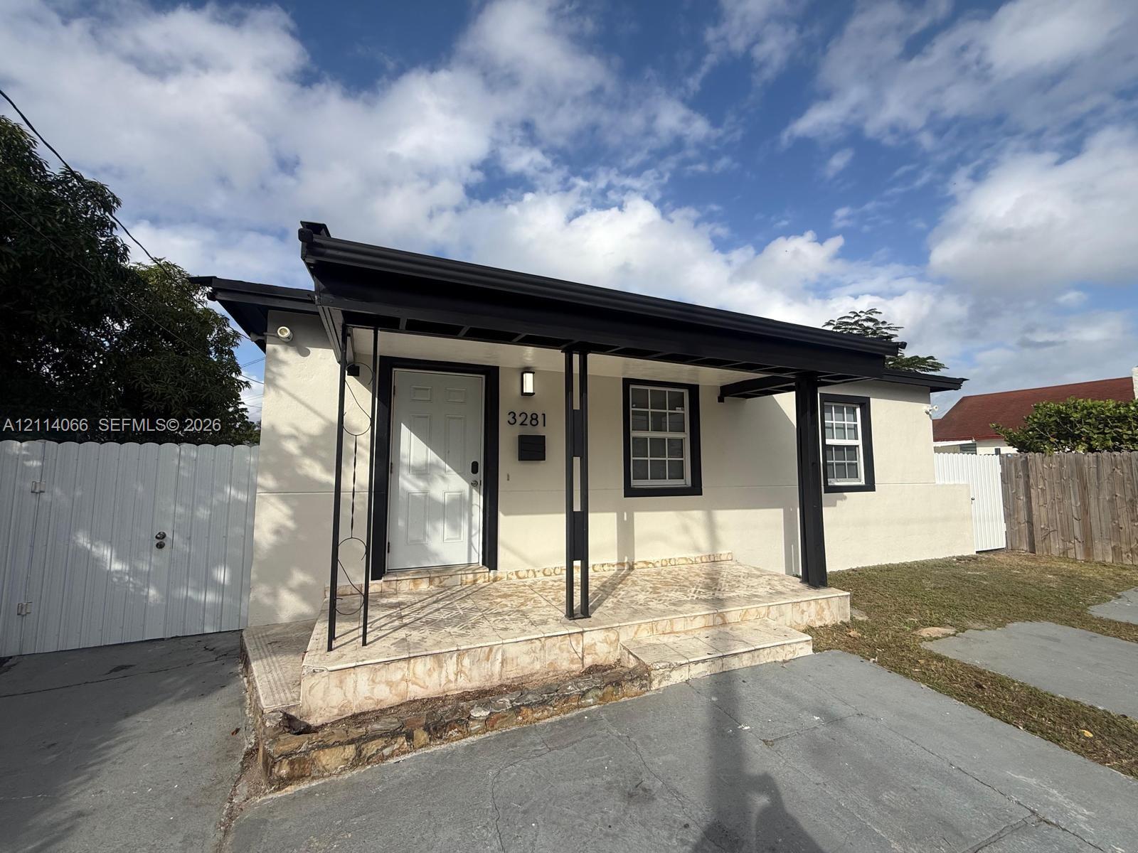 Stucco exterior with a covered porch featuring stone-tiled flooring and black metal support columns