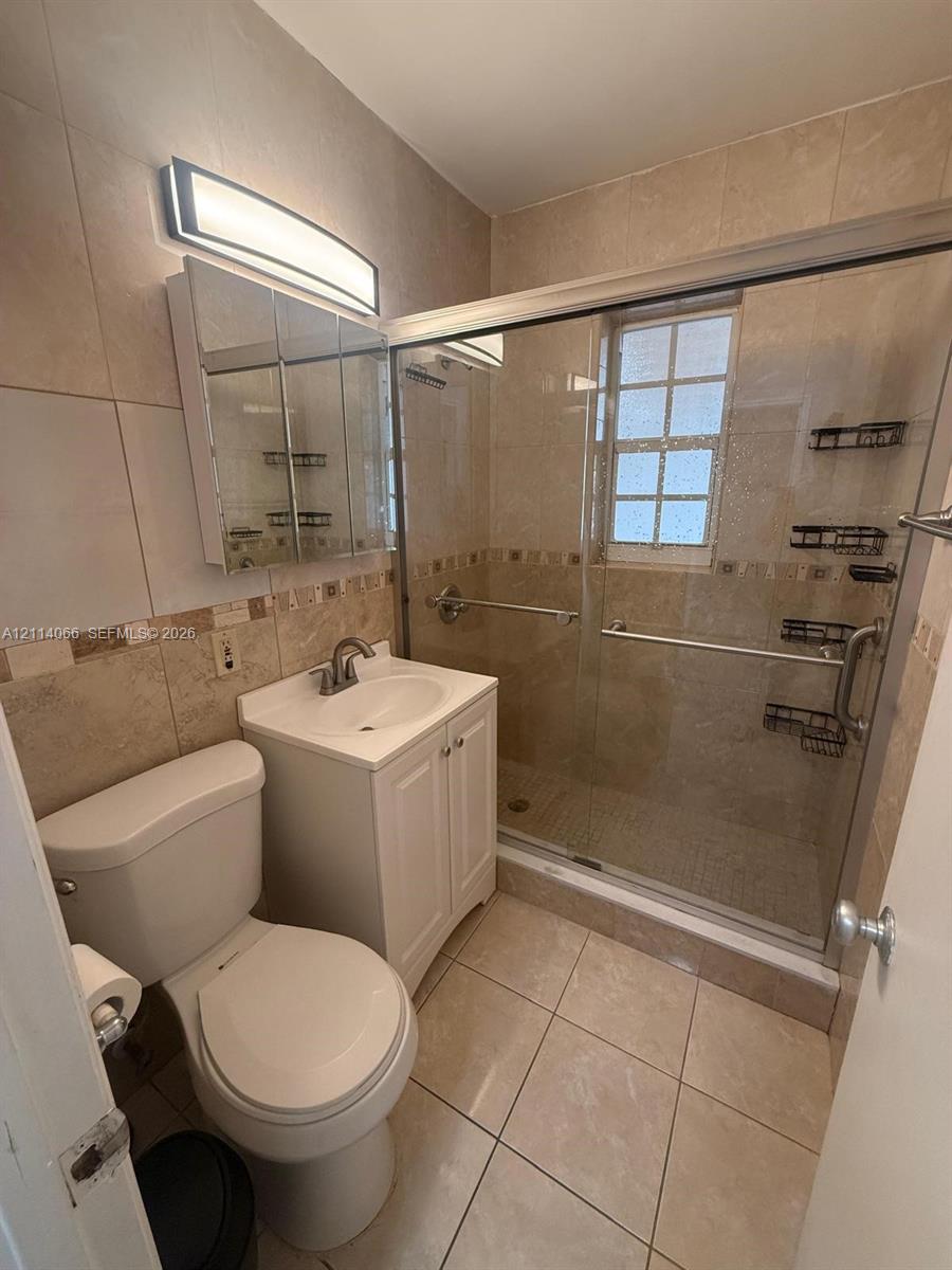 Bathroom featuring a glass-enclosed shower, tiled walls with a decorative accent border, a pedestal-style vanity with white cabinetry, and a mirrored medicine cabinet