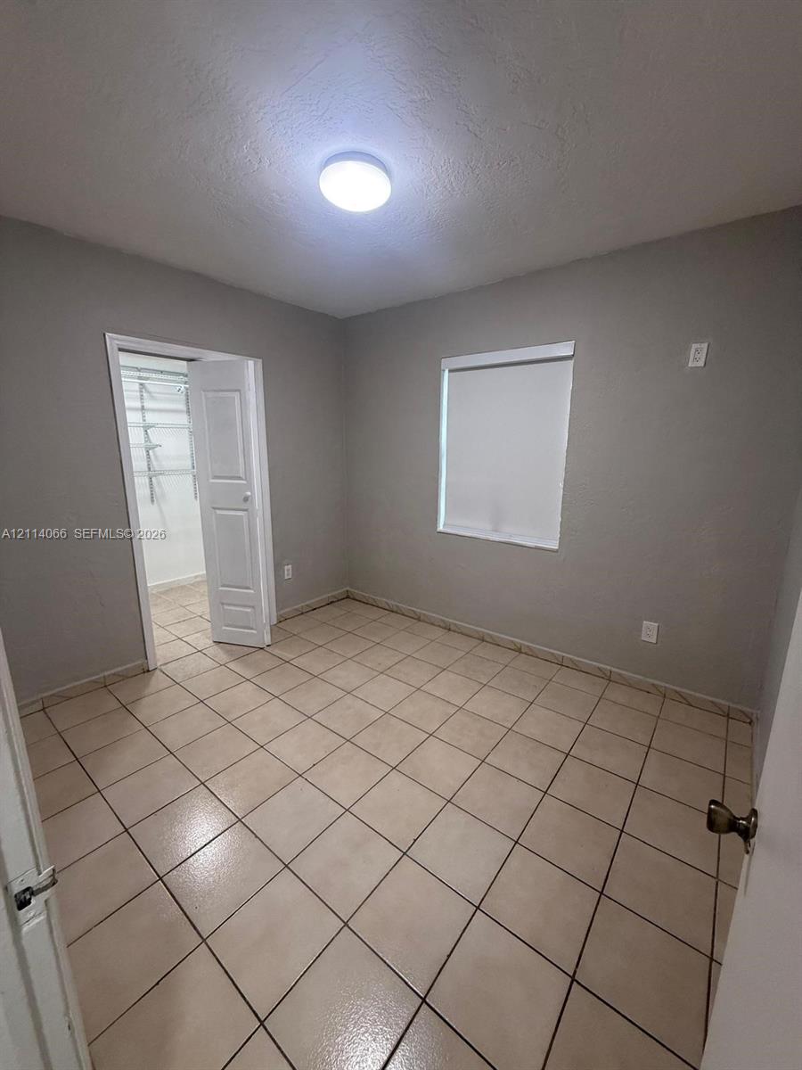 Room featuring neutral-toned ceramic tile flooring, a walk-in closet with built-in shelving, a recessed light fixture, and a single-hung window with a roller shade