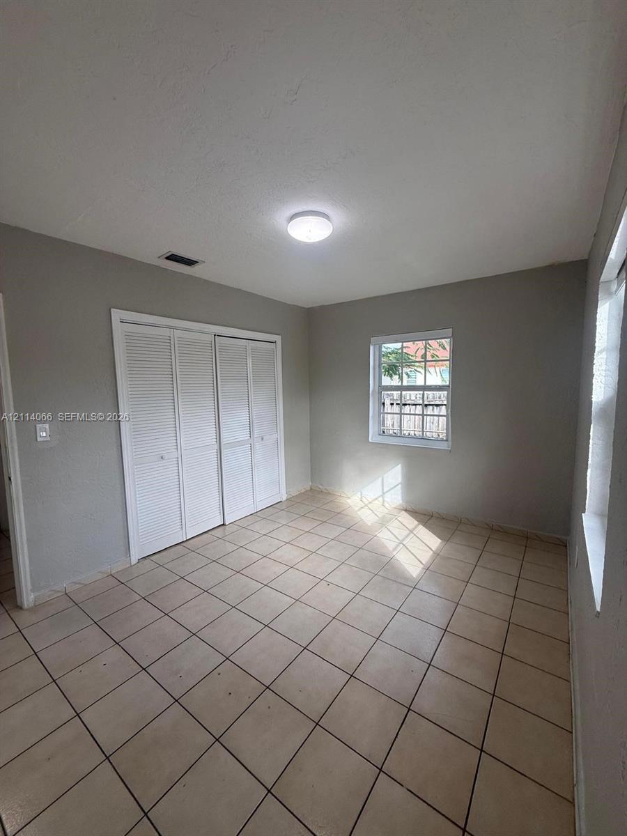 Neutral-toned interior featuring ceramic tile flooring, built-in closet with louvered doors, and multi-pane windows