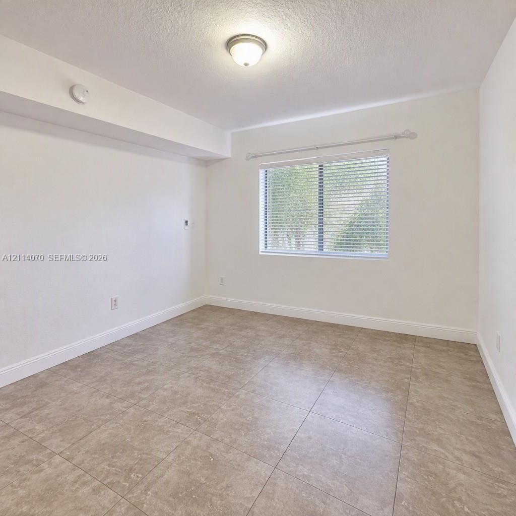 Neutral-toned tiled flooring, wall-mounted light fixture, and window with adjustable blinds