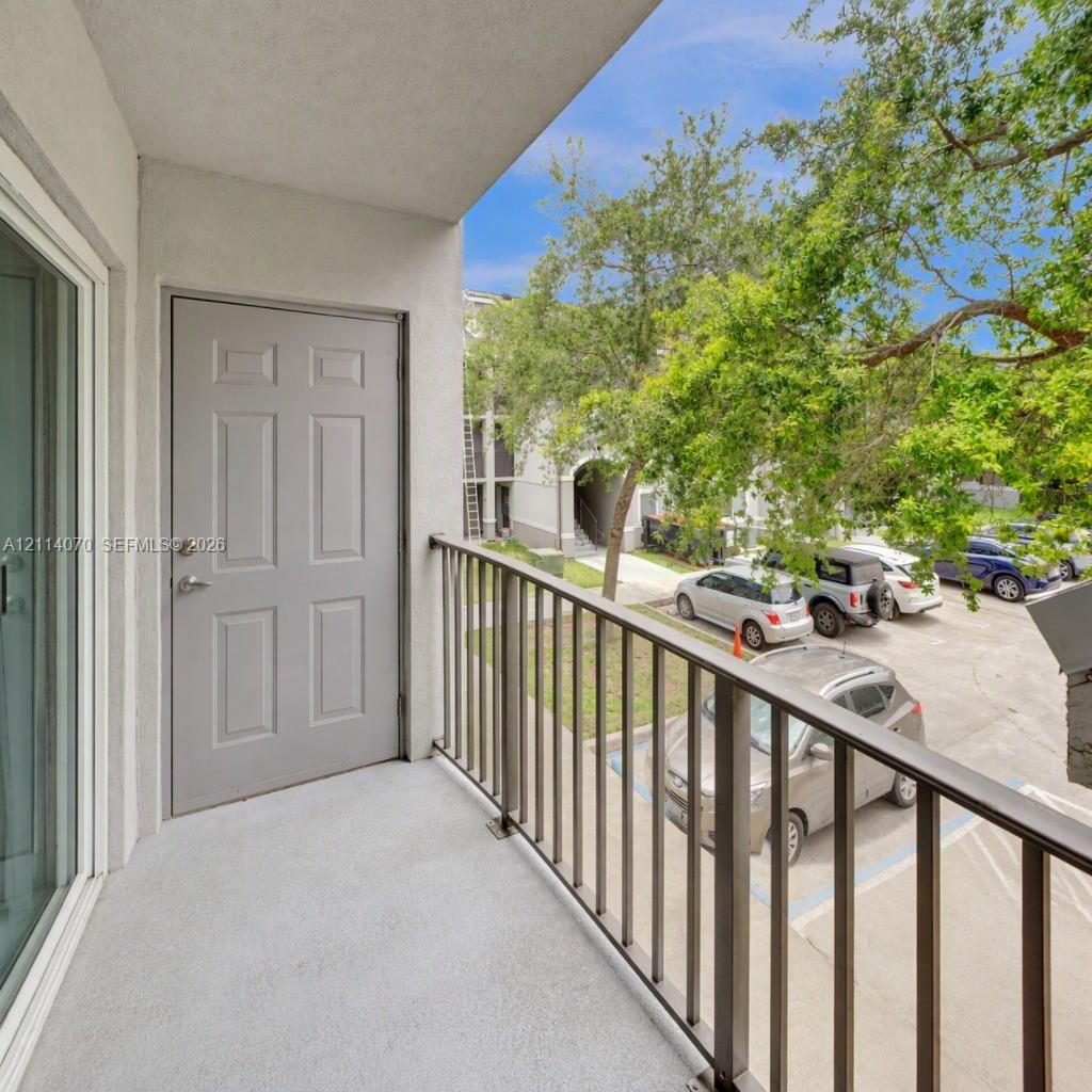 Covered balcony featuring concrete flooring, a paneled door, and metal railing