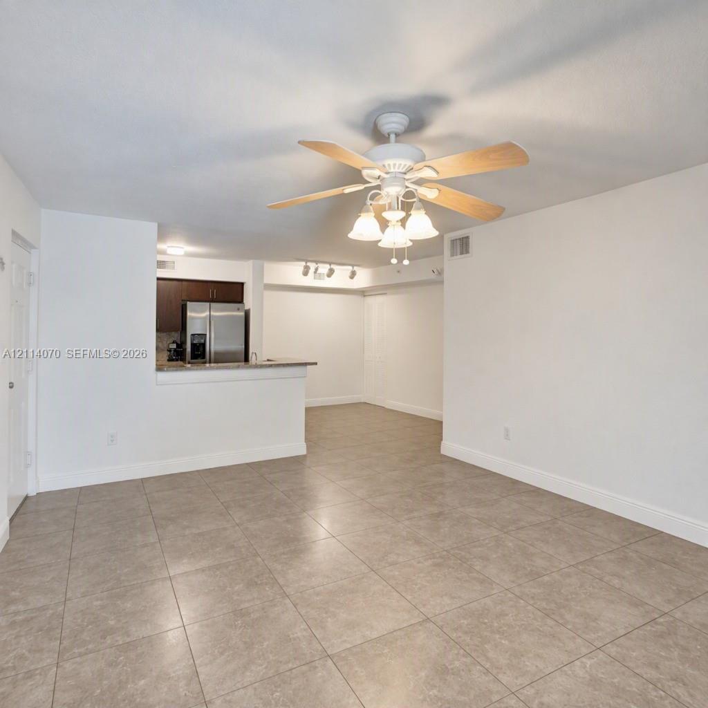 Large-format tile flooring, central ceiling fan with multi-light fixture, breakfast bar, and stainless steel refrigerator