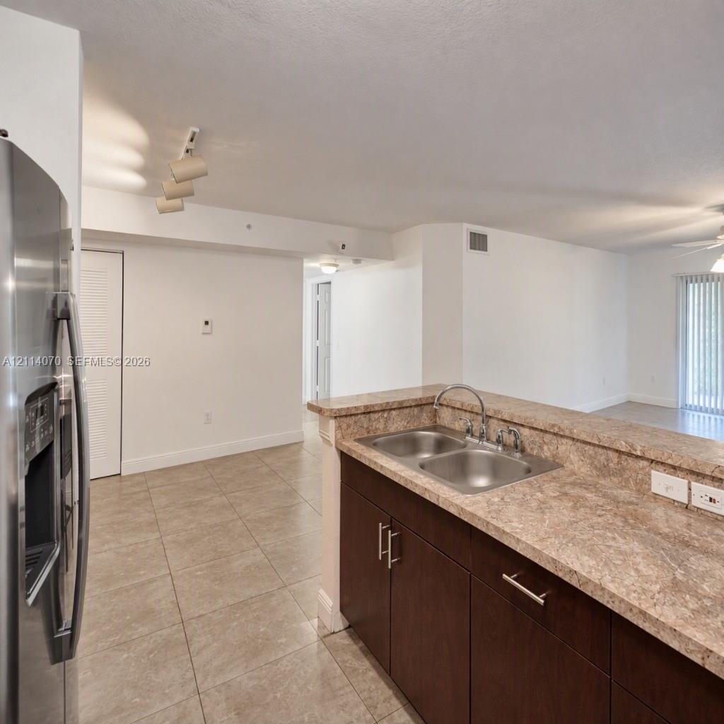 Kitchen featuring dark wood-finish cabinetry, stone-texture countertops, stainless steel dual-basin sink, and tile flooring