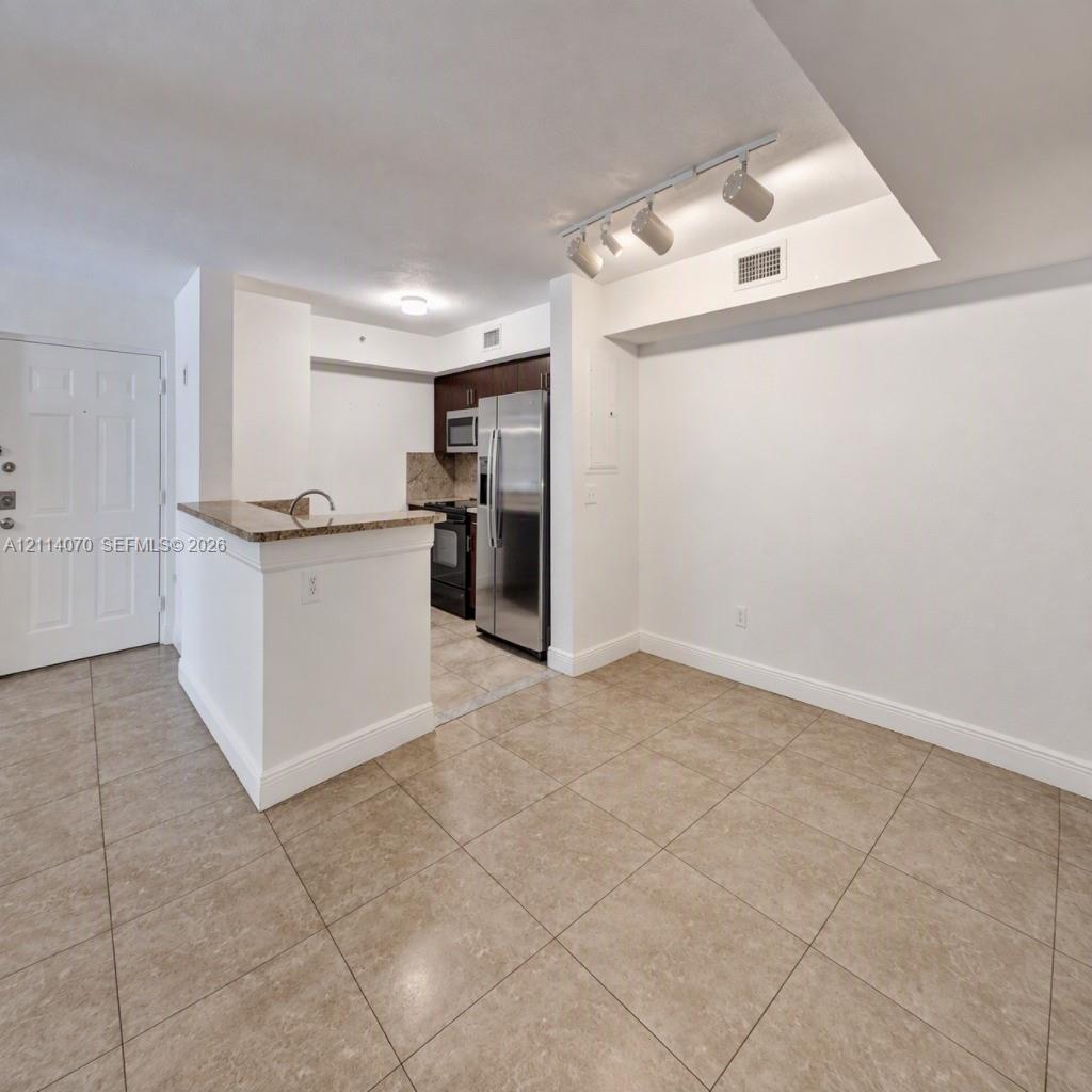Kitchen featuring stainless steel appliances, dark wood-finish cabinetry, stone-surfaced breakfast bar, and tile flooring throughout