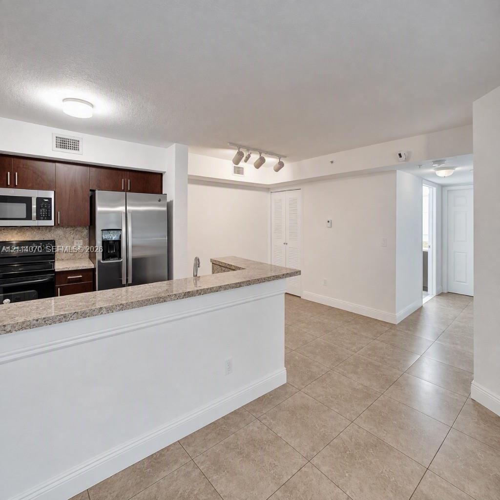 Kitchen featuring dark wood cabinetry, stone-finish countertops, stainless steel appliances, a peninsula with a sink, and tile flooring
