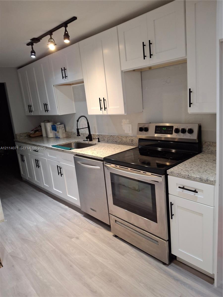 Kitchen featuring shaker-style white cabinetry with matte black hardware, light stone-patterned countertops, stainless steel appliances, a high-arc black faucet, and track lighting