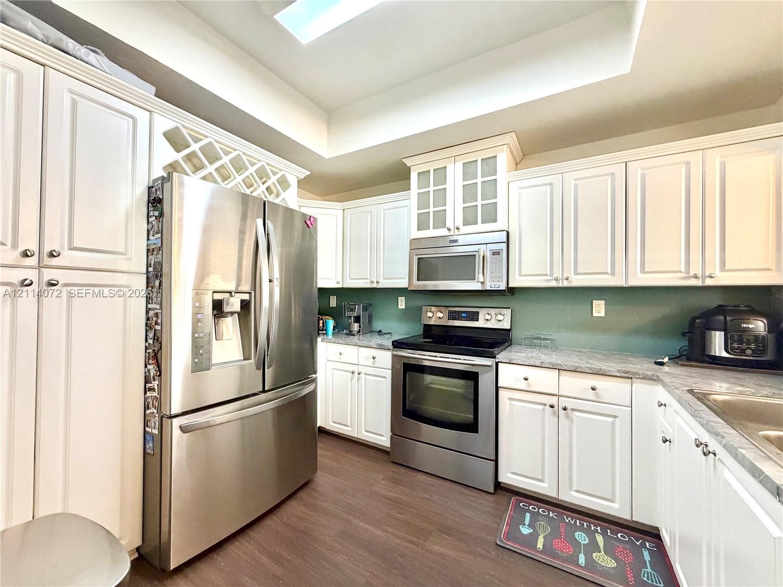 Kitchen featuring white cabinetry with integrated wine storage, stainless steel appliances, stone-finish countertops, and wood-finish flooring