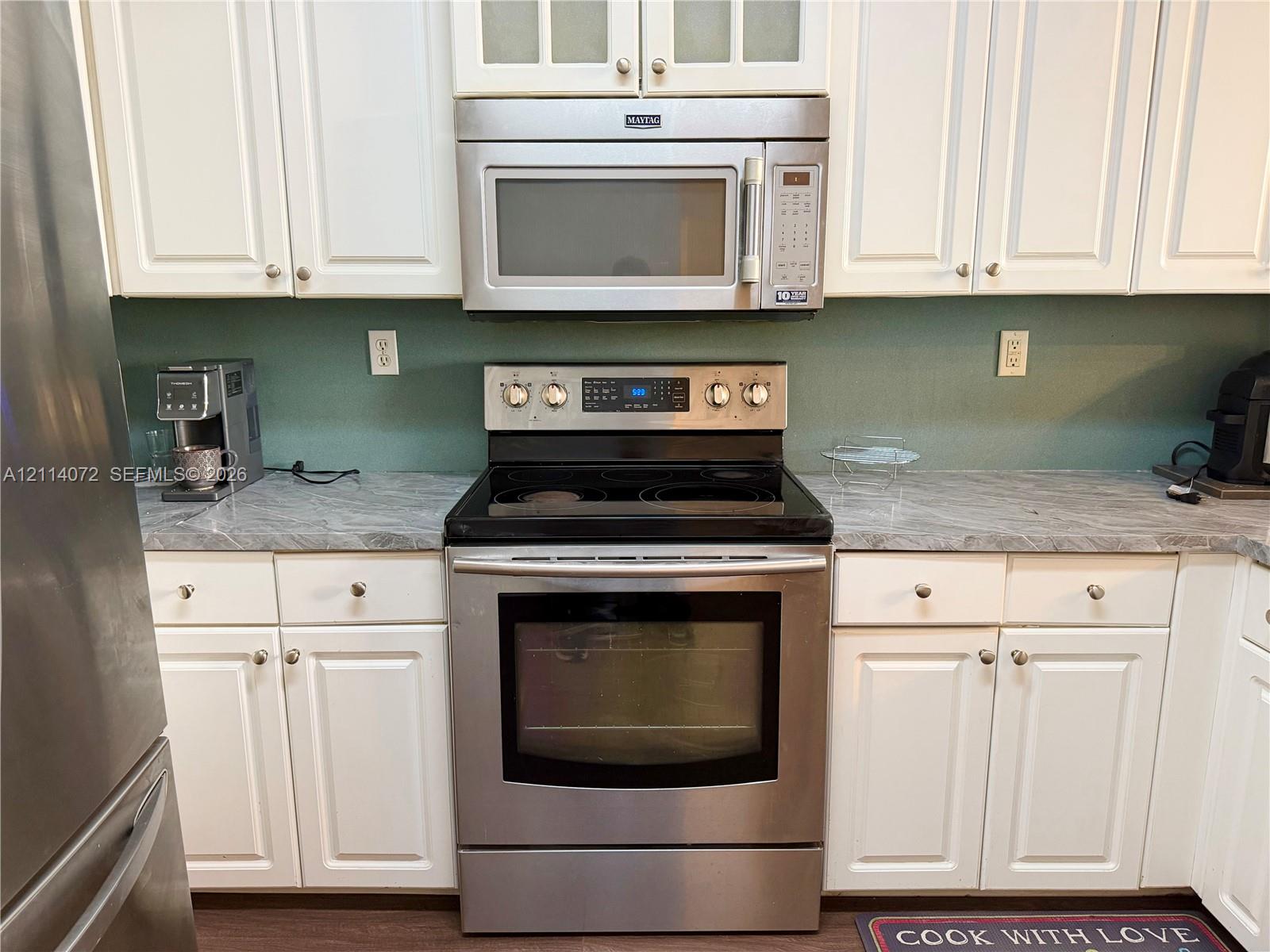Kitchen featuring white shaker-style cabinetry, stone-patterned laminate countertops, stainless steel electric range, and stainless steel over-the-range microwave
