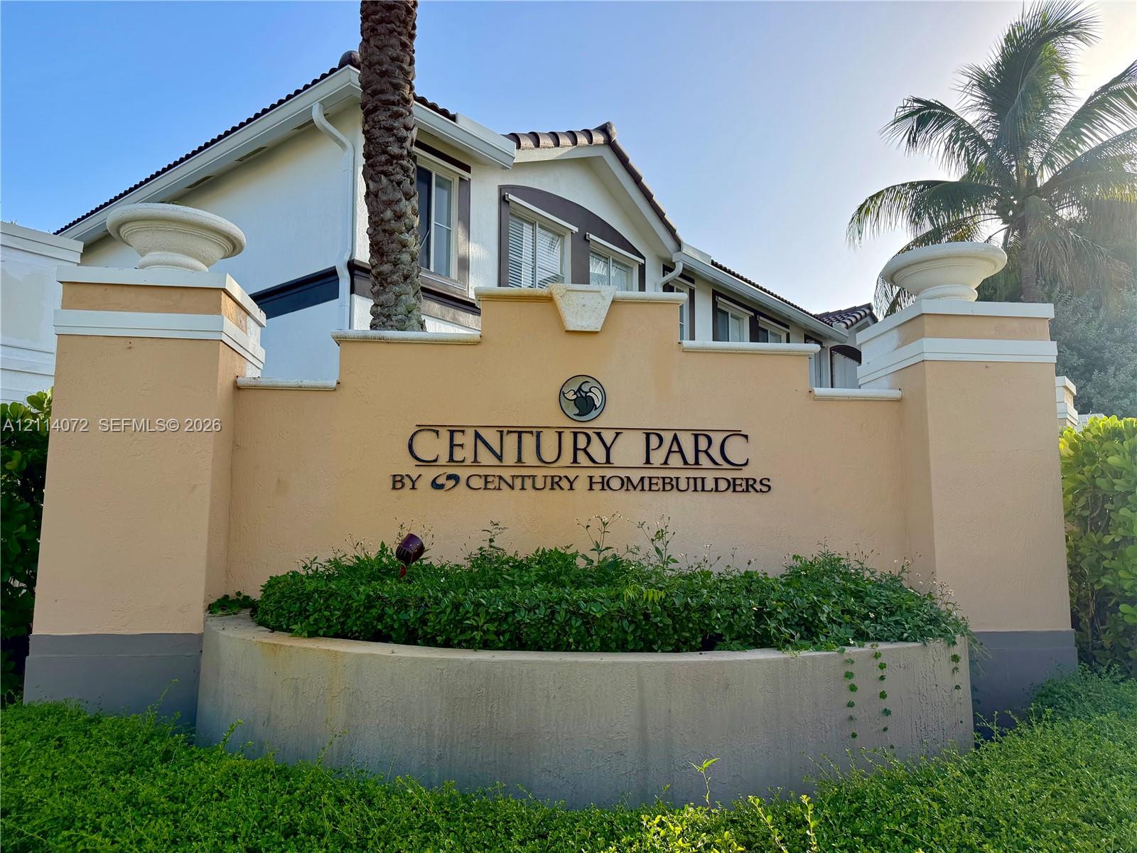Stucco masonry monument signage featuring dual stone-capped columns, integrated concrete planter, and professional landscape hedging