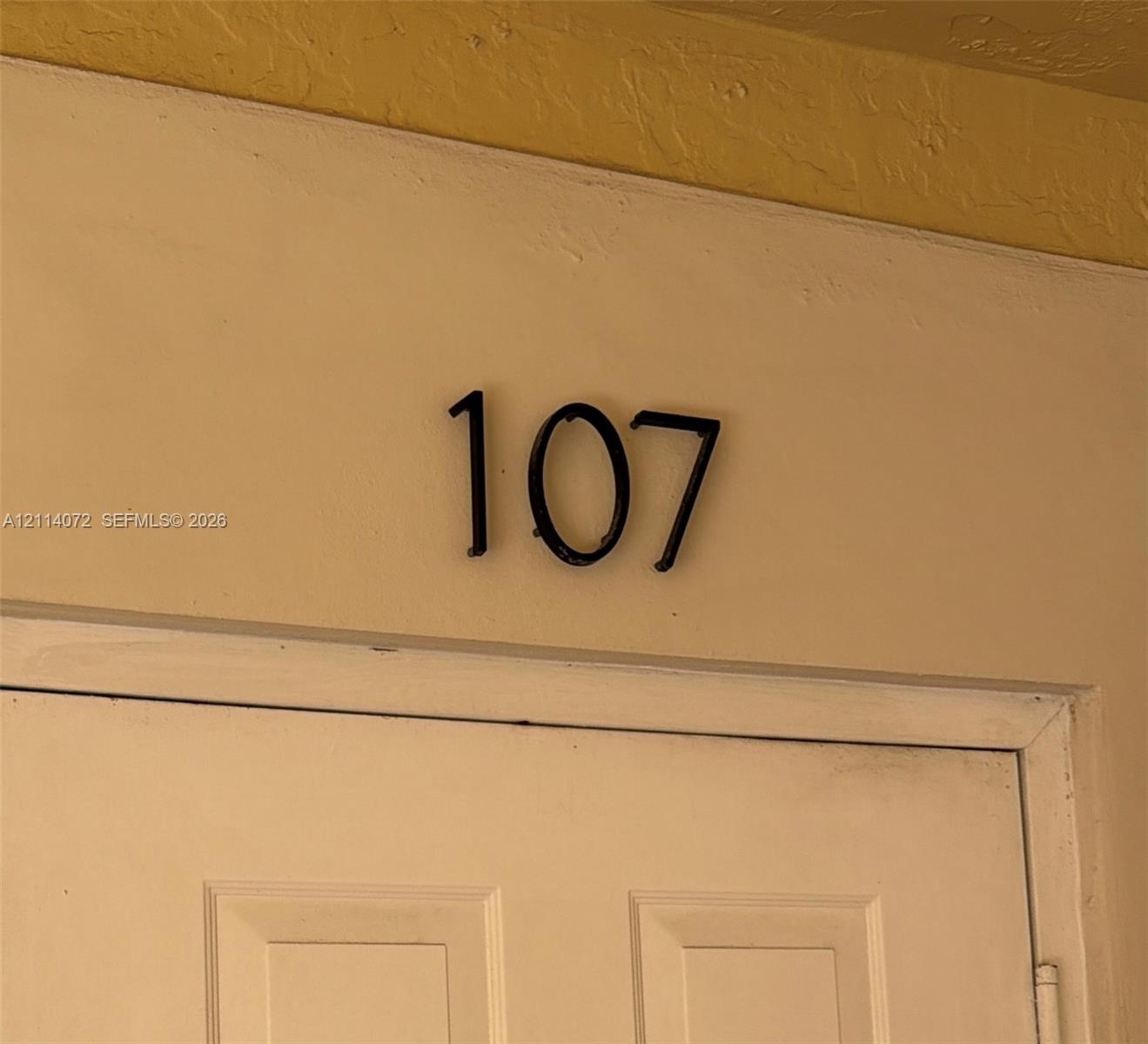 Matte black numeric address signage mounted on a neutral-toned exterior wall above a paneled door