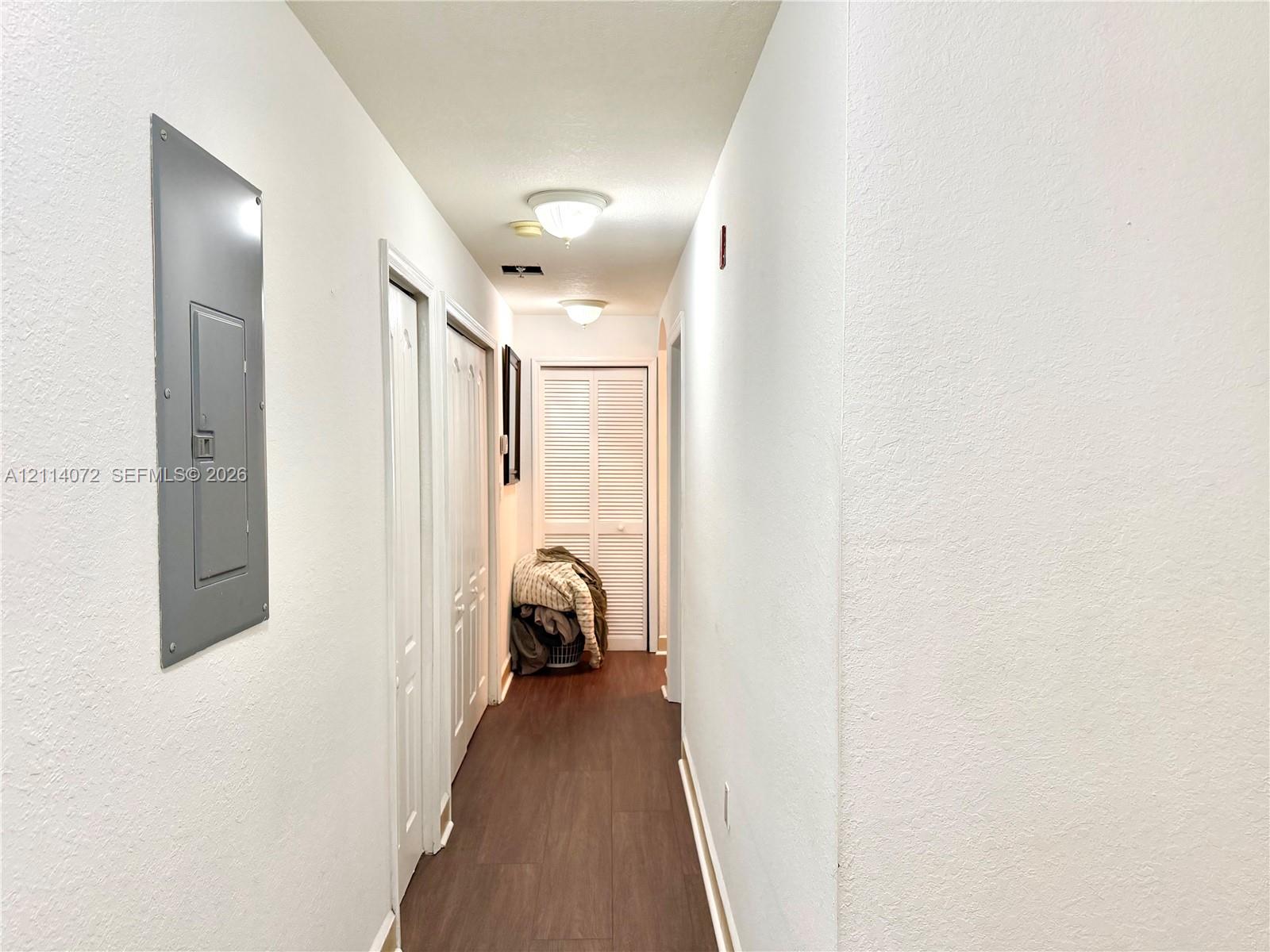 Interior hallway featuring wood-finish flooring, two sets of louvered closet doors, and flush-mount ceiling lighting