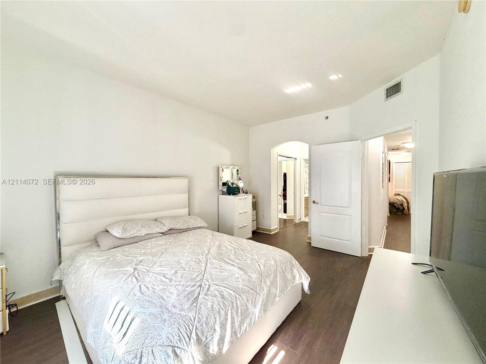 Wood-finish flooring, high ceilings, and an arched doorway featuring a multi-panel door