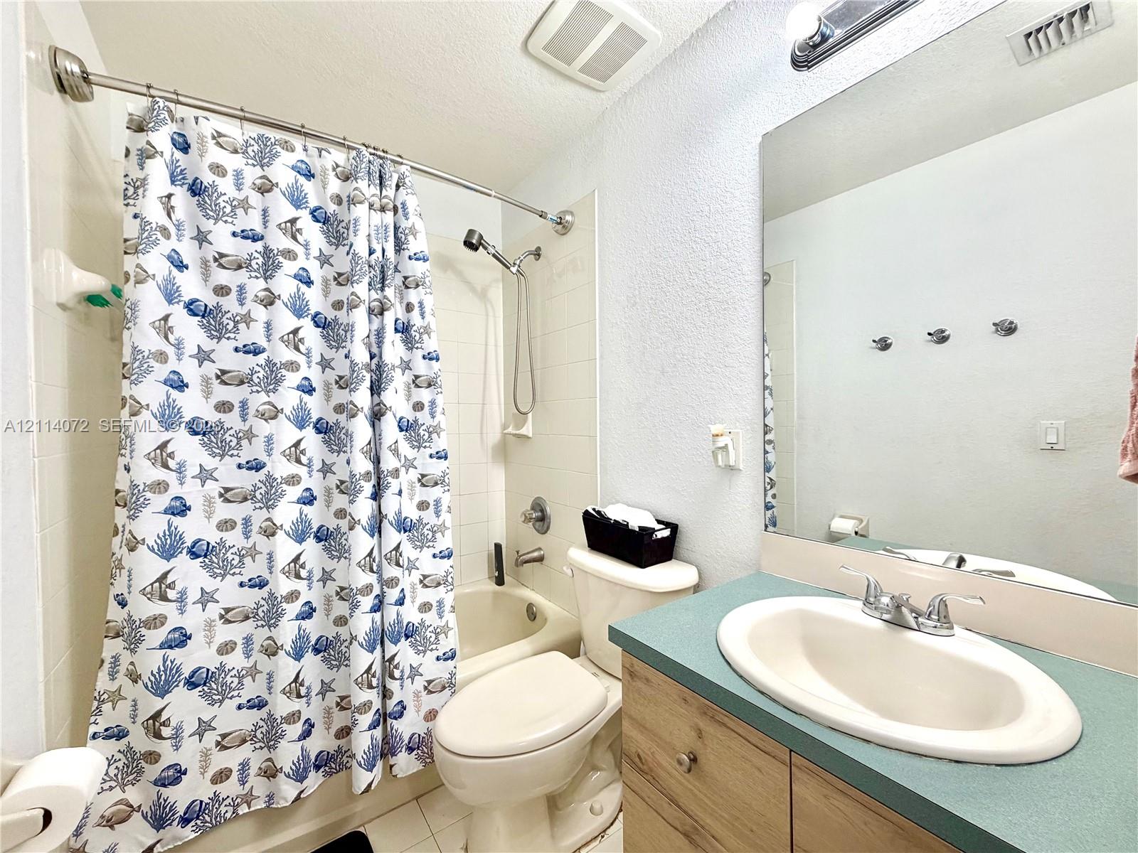Bathroom featuring a wood-finish vanity cabinet, solid-surface countertop with an integrated oval sink, and a full-width vanity mirror