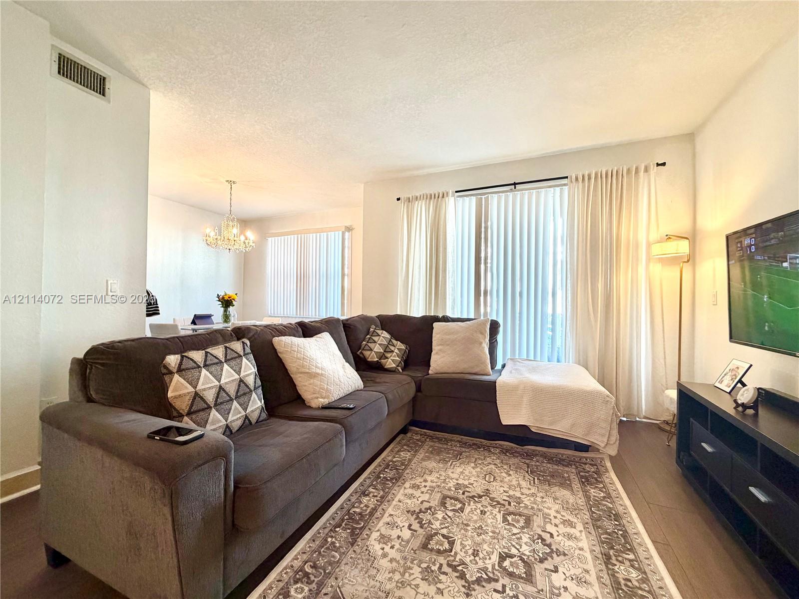 Living space featuring wood-finish flooring, floor-to-ceiling sliding glass doors with vertical blinds, and a traditional-style chandelier