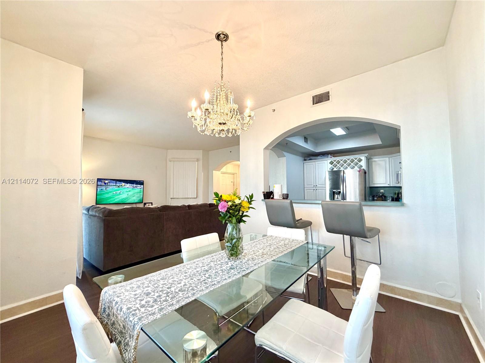 Dining area featuring wood-finish flooring, an ornate crystal chandelier, and a decorative arched pass-through window with a built-in breakfast bar