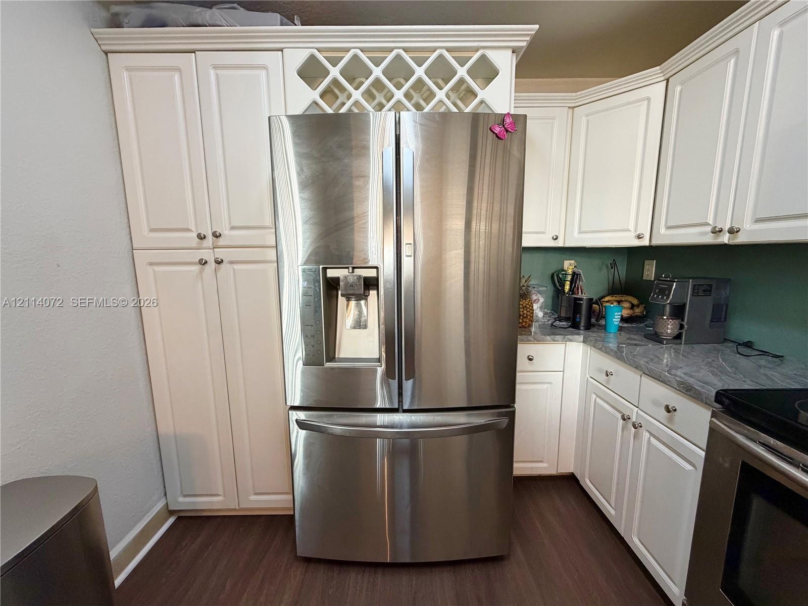 Kitchen featuring white shaker-style cabinetry, stainless steel French-door refrigerator, integrated wine rack, stone-finish countertops, and wood-finish flooring