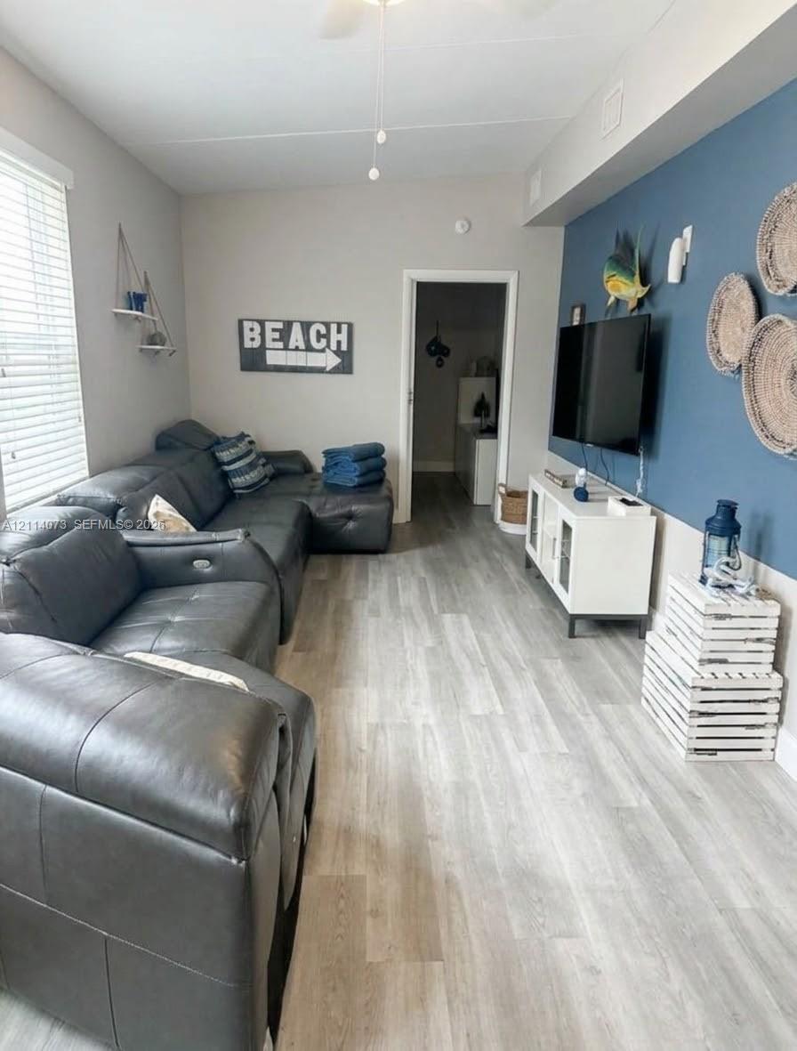 Living area featuring wood-finish flooring, a bold blue accent wall, and horizontal blinds Living area featuring wood-finish flooring, a bold blue accent wall, and horizontal blinds