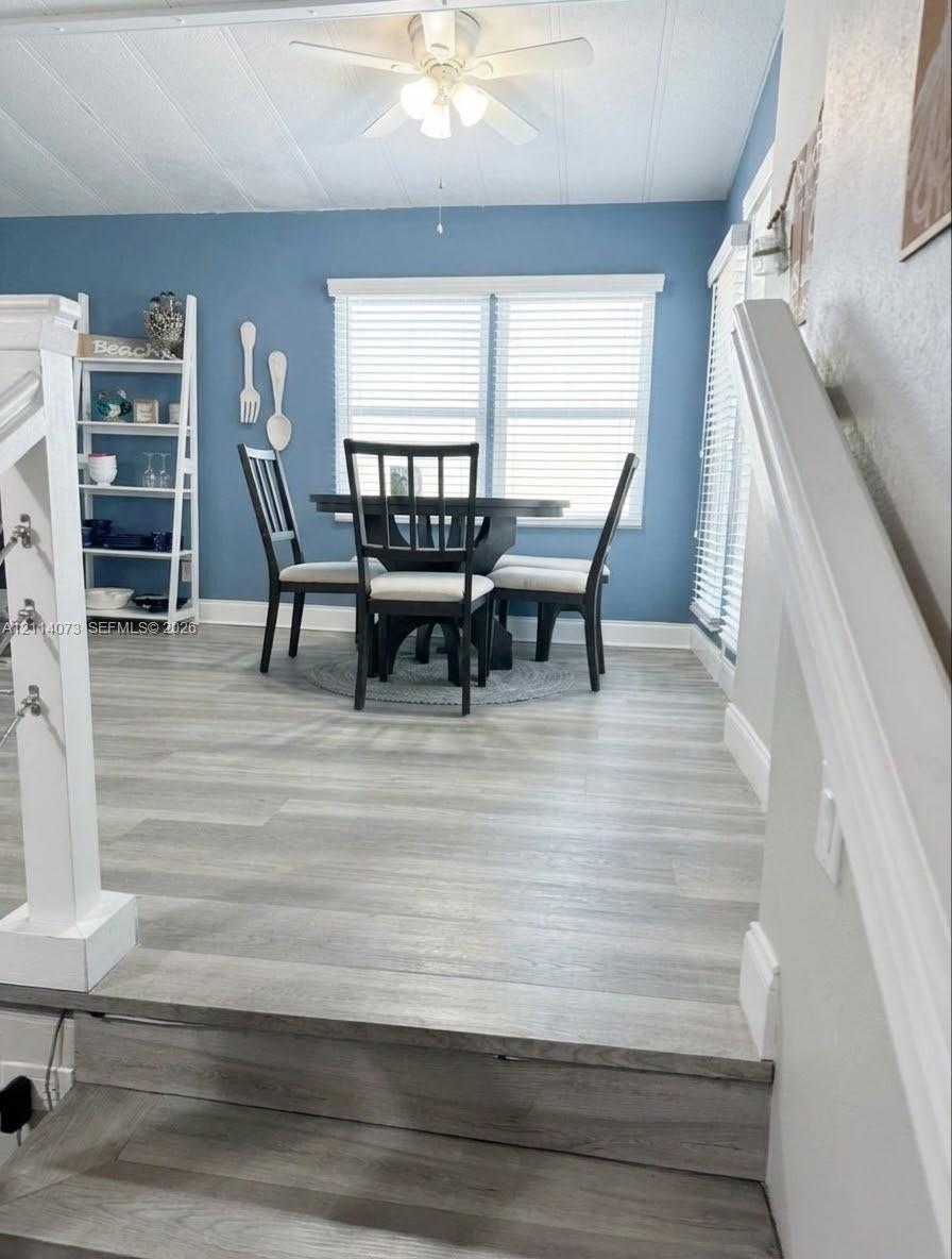 Wood-finish flooring, white ceiling fan with integrated lighting, dual windows with horizontal blinds, and a white stair railing with cable accents Wood-finish flooring, white ceiling fan with integrated lighting, dual windows with horizontal blinds, and a white stair railing with cable accents