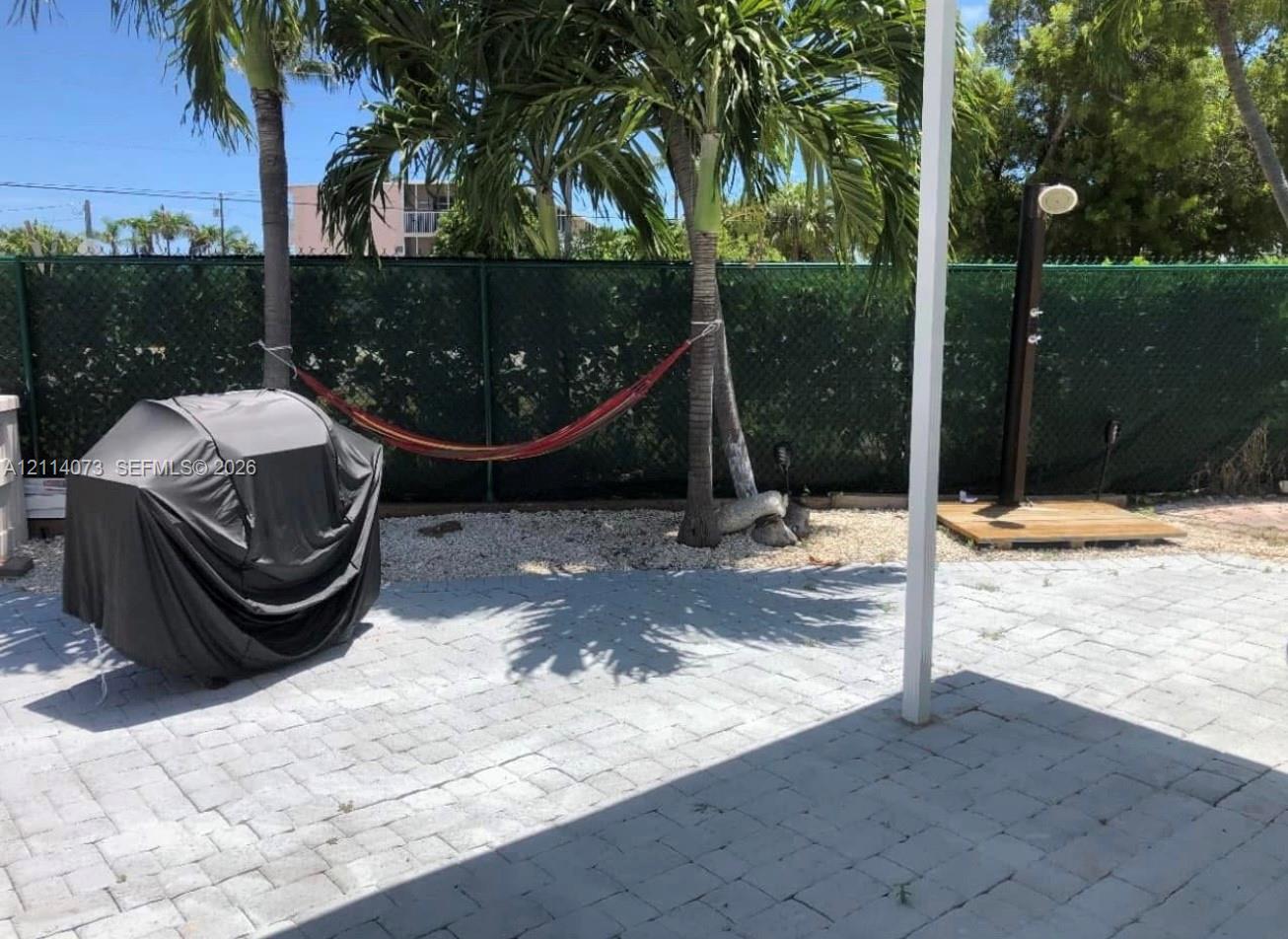 Outdoor patio featuring gray paver hardscaping, an open-air shower with a wooden platform, and mature palm trees Outdoor patio featuring gray paver hardscaping, an open-air shower with a wooden platform, and mature palm trees