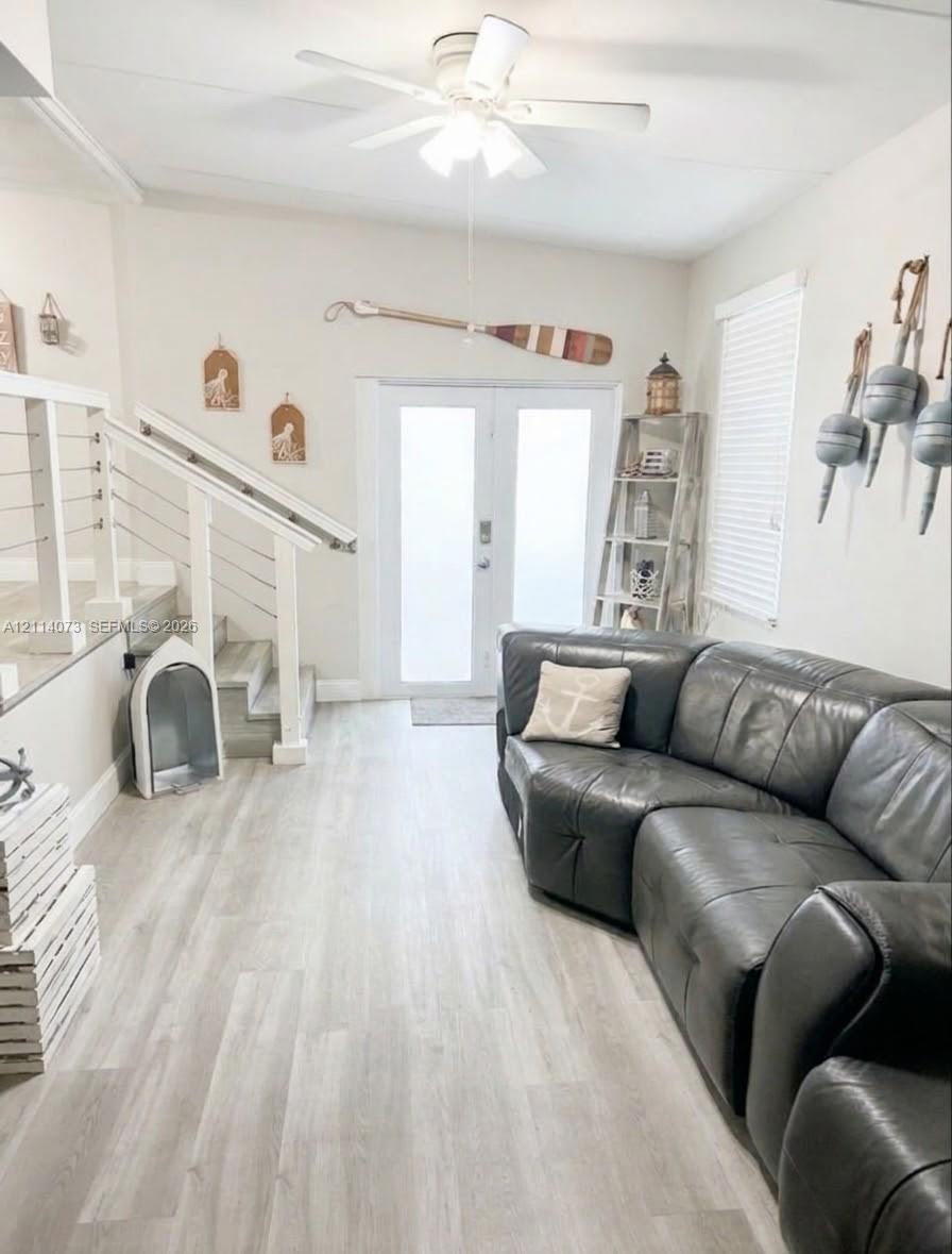 Double entry doors with frosted glass panels, wood-finish flooring, staircase with white railing and cable balusters, and a ceiling-mounted light fixture with fan Double entry doors with frosted glass panels, wood-finish flooring, staircase with white railing and cable balusters, and a ceiling-mounted light fixture with fan