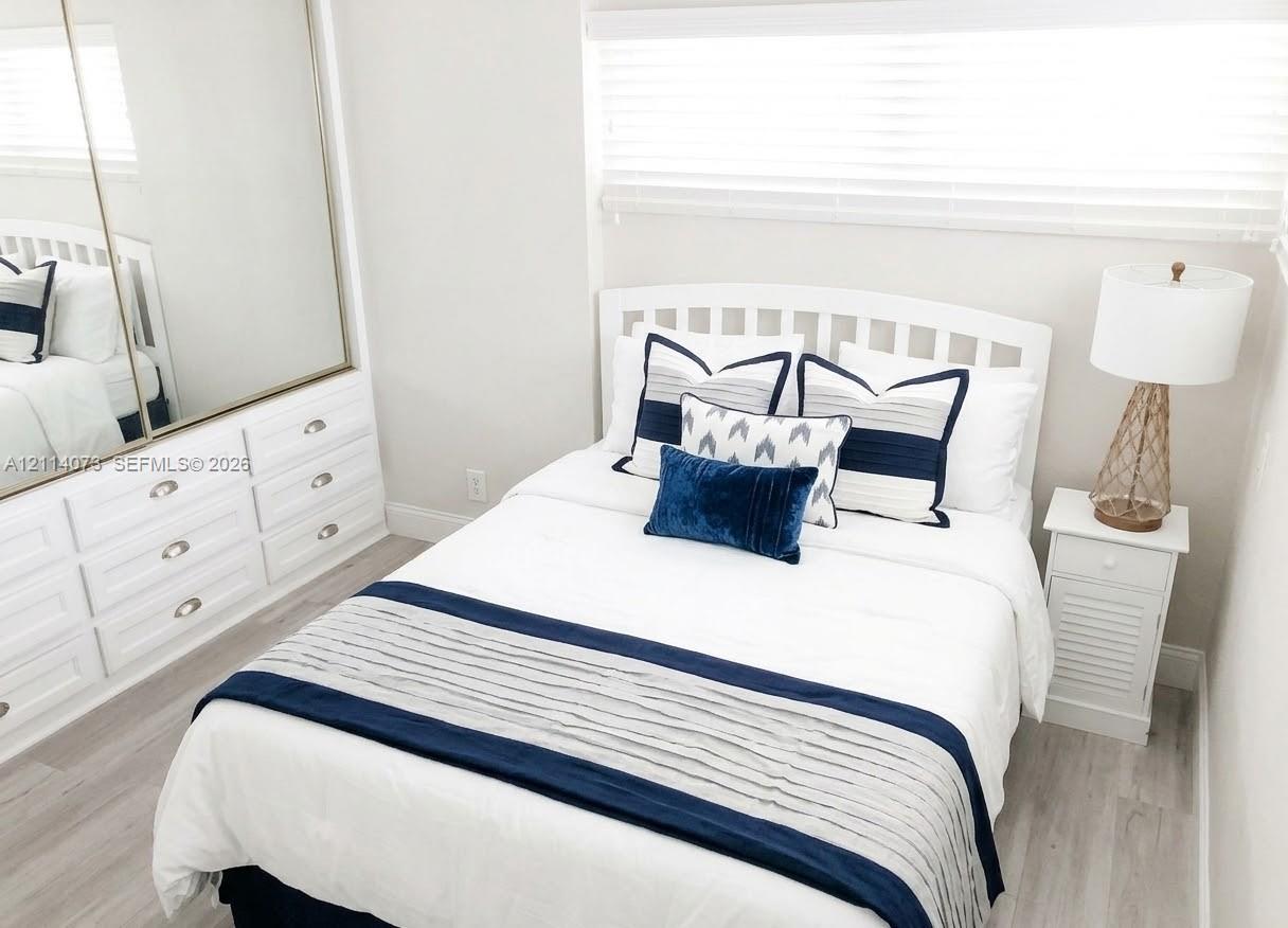 Built-in cabinetry featuring white shaker-style drawers, mirrored sliding closet doors, wood-finish flooring, and horizontal window blinds Built-in cabinetry featuring white shaker-style drawers, mirrored sliding closet doors, wood-finish flooring, and horizontal window blinds