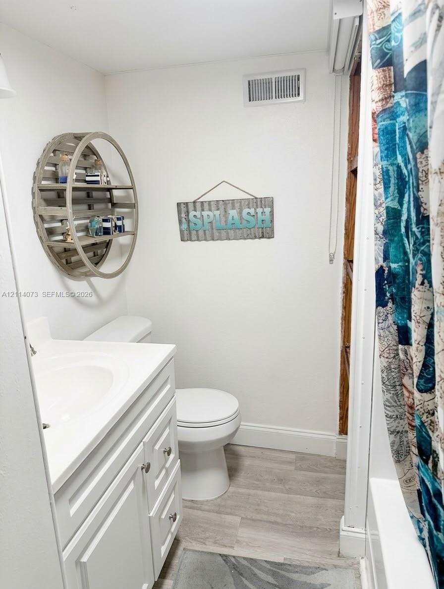 Bathroom featuring a white vanity cabinet with a integrated sink, wood-finish flooring, and a tub-shower combination Bathroom featuring a white vanity cabinet with a integrated sink, wood-finish flooring, and a tub-shower combination
