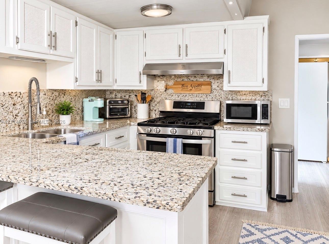Kitchen featuring white cabinetry with textured door panels, stone-finish countertops, stainless steel appliances including a gas range, and a high-arc pull-down faucet Kitchen featuring white cabinetry with textured door panels, stone-finish countertops, stainless steel appliances including a gas range, and a high-arc pull-down faucet