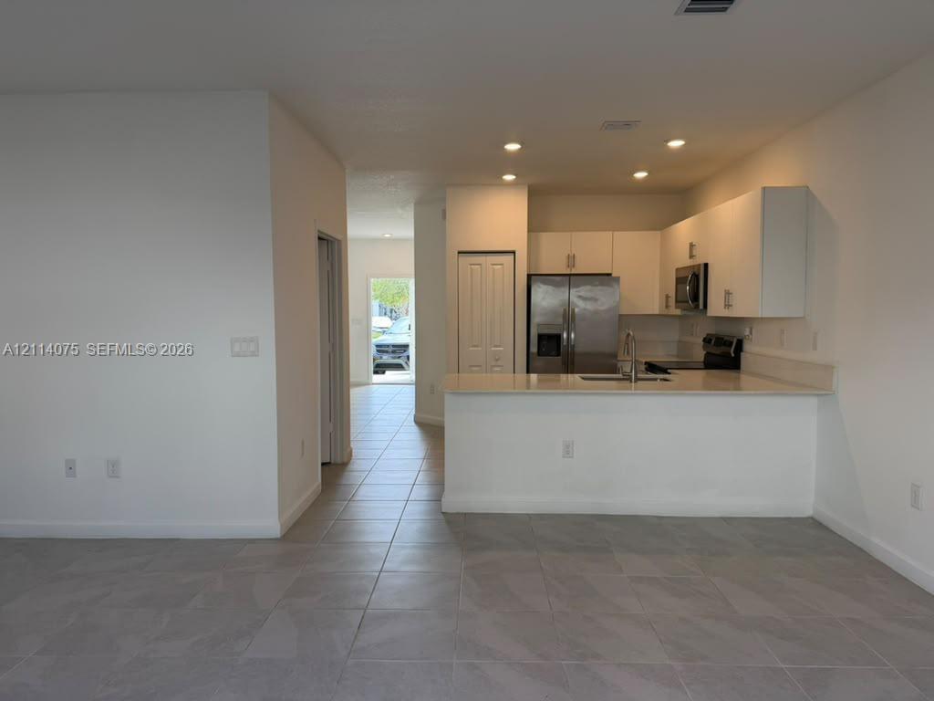 Kitchen featuring white flat-panel cabinetry, light-toned stone-surface countertops, stainless steel appliances, recessed ceiling lighting, and tile flooring