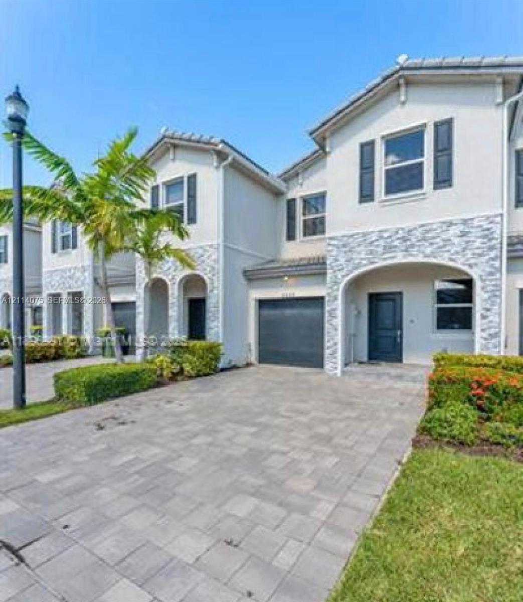 Multi-level exterior featuring stucco siding, stone veneer accents, arched entryways, integrated garage, and paver driveway