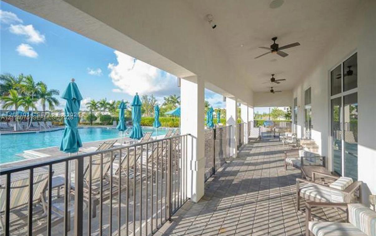 Covered patio featuring paver flooring, multiple ceiling fans, and a metal perimeter fence overlooking a swimming pool