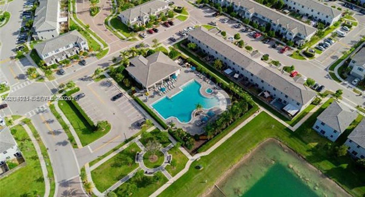 Aerial perspective of community center featuring a swimming pool, attached spa, covered patio pavilion, paved walking paths, and a retention pond