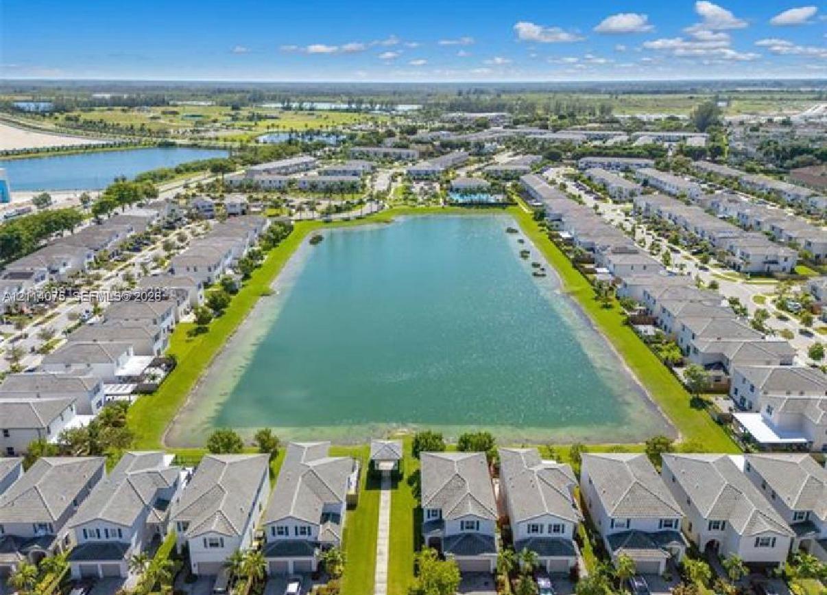 Aerial perspective of a planned community featuring a large central retention lake, manicured green space, paved pedestrian pathways, and a lakeside gazebo