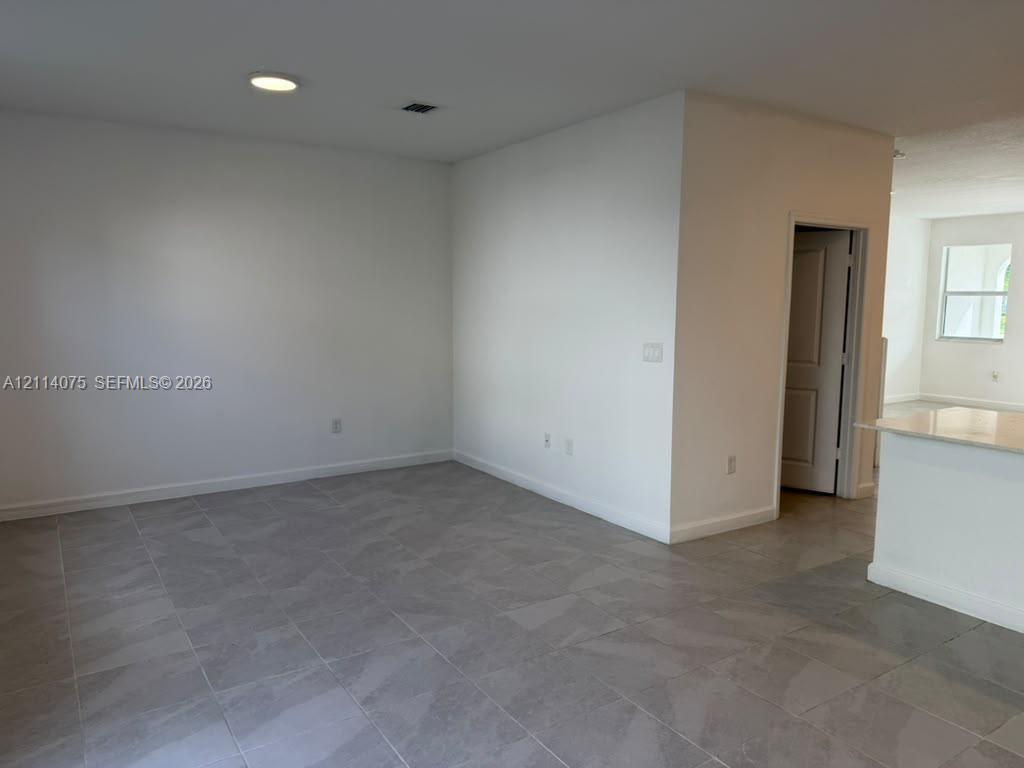Neutral interior space featuring large-format ceramic tile flooring, recessed lighting, and a kitchen island with a stone-finish countertop