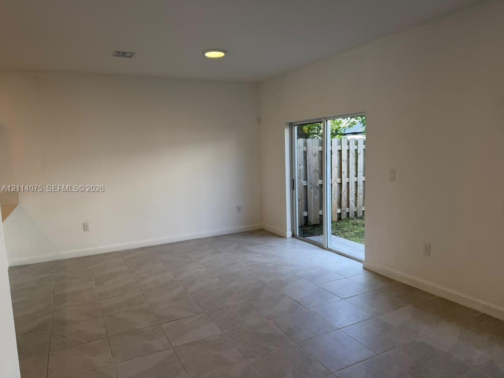 Interior space featuring large-format neutral floor tile, recessed ceiling lighting, and sliding glass doors opening to a fenced outdoor area