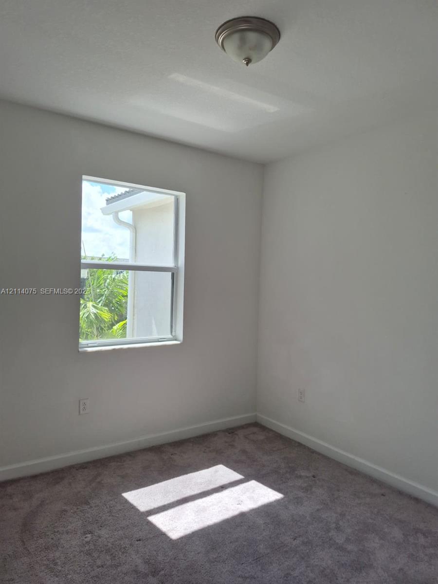 Neutral-toned interior room featuring wall-to-wall carpeting, a single-hung window, and a flush-mount ceiling light fixture