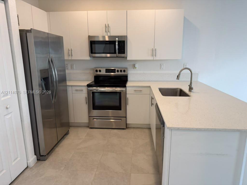 Kitchen featuring white cabinetry, quartz countertops, stainless steel appliances, and tile flooring