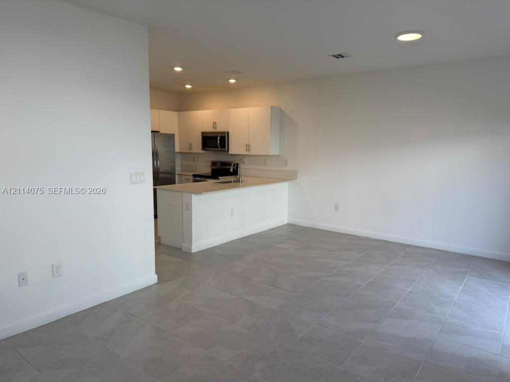 Kitchen featuring white cabinetry, solid-surface countertops, stainless steel appliances, and large-format tile flooring
