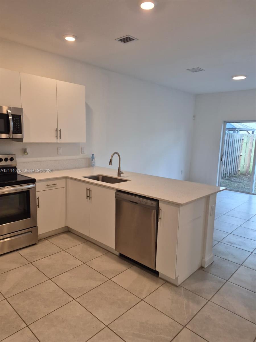 Kitchen featuring white cabinetry, light-toned stone-finish countertops, stainless steel appliances, recessed ceiling lighting, and tile flooring