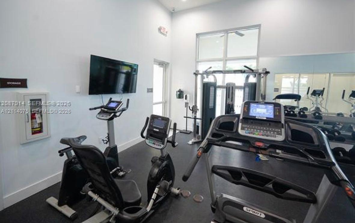 Fitness center featuring rubber flooring, large wall-mounted mirrors, high ceilings with clerestory windows, and a wall-mounted television