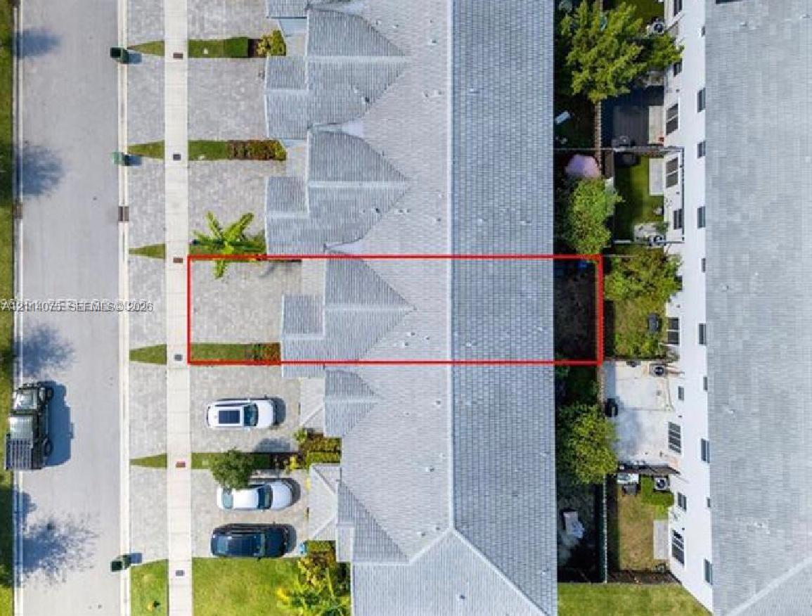 Aerial perspective of a multi-unit property featuring a paver driveway, shingle roofing, and a private rear ground-level patio space